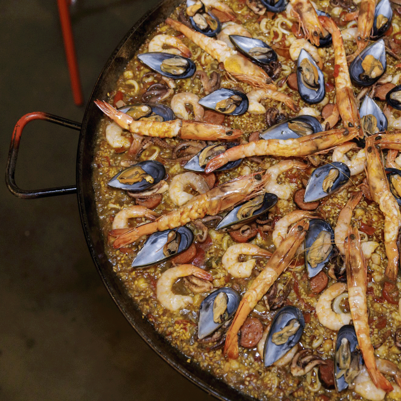 A vibrant paella cooked in a giant pan with saffron rice, fresh seafood, and lemon wedges.